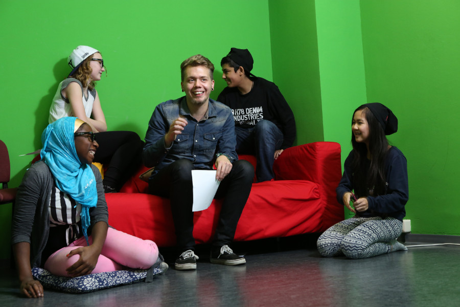 Ein Freiwilliger mit vier Jugendlichen in einem grün gestrichenem Raum. Einige sitzen auf einem roten Sofa, zwei junge Frauen hocken auf dem Boden davor.
