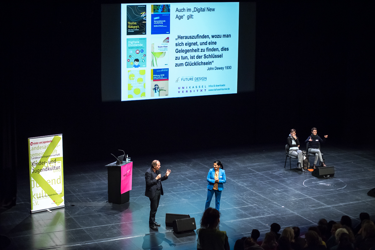 Foto: von oben auf die Bühne, dort sprechen Prof. Dr. Olaf-Axel Burow und Prasanna Oommen miteinander