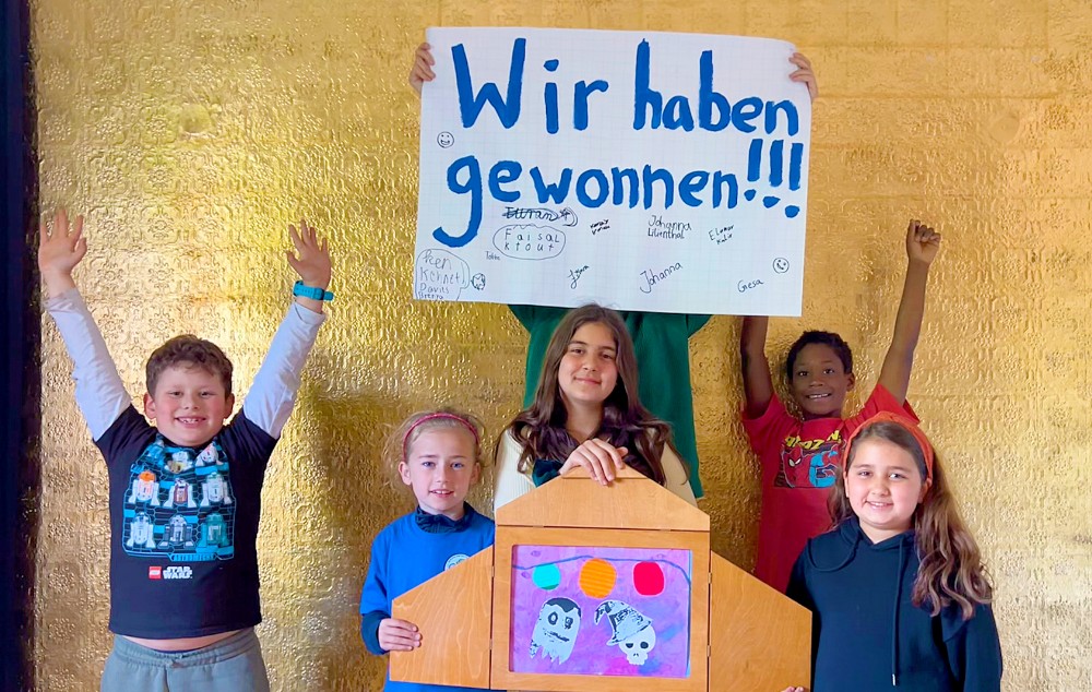 6 Kinder, davon hält eins ein Schild hoch, darauf steht "Wir haben gewonnen!".