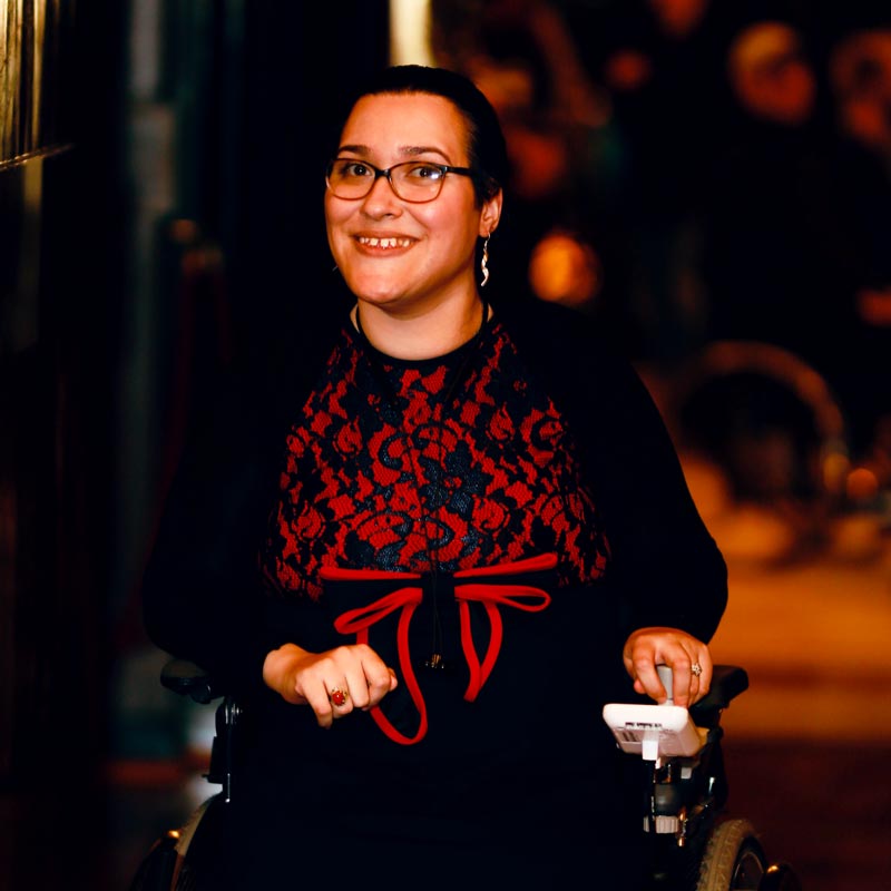 Porträt von Hiba:  lächelnde Frau mit Brille und Rollstuhl