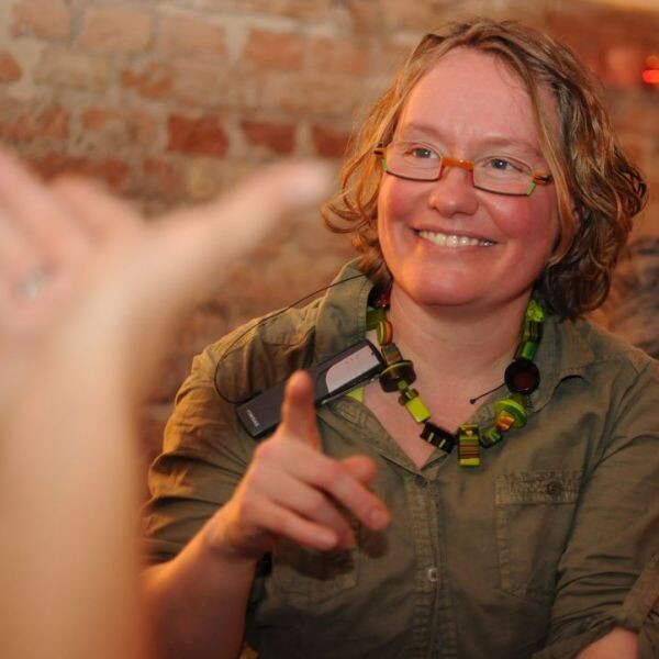 Portrait von Ines Helke, lockige kurze Haare, bunte Brille und breites Lächeln